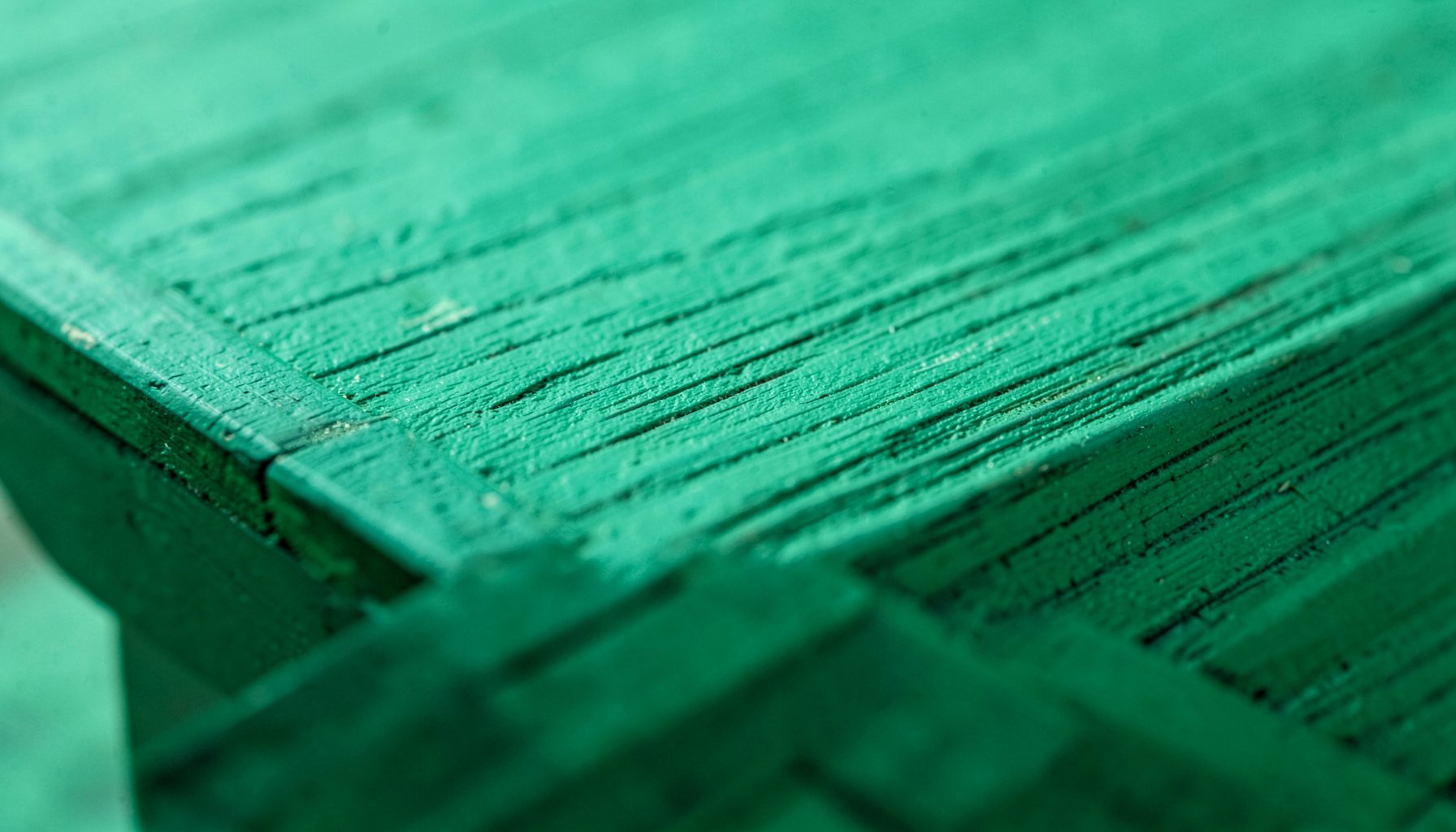 Primissimo piano di un bordo di legno dipinto in verde acqua che mostra le venature, atmosfera calma e materica.