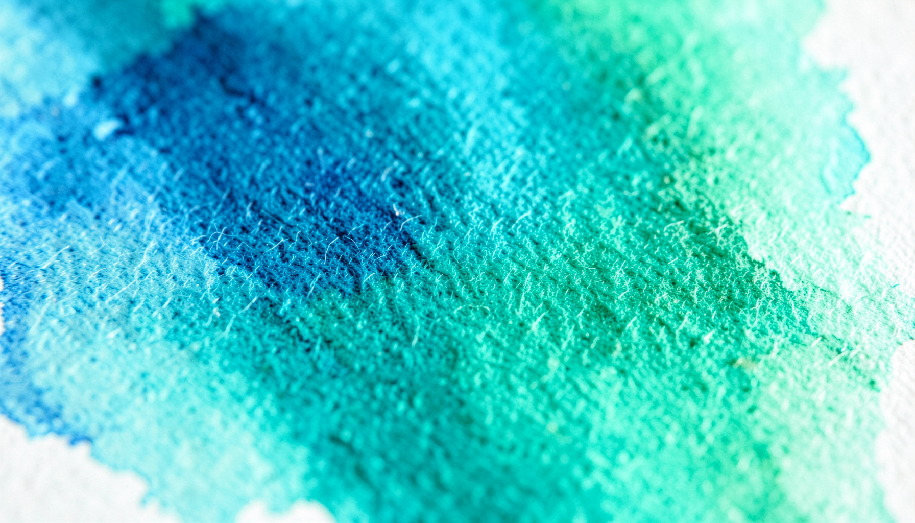 Primissimo piano di carta da acquerello bagnata con pigmenti blu e verdi che si fondono in morbide velature, texture fibrosa e luminosa, atmosfera silenziosa e creativa.